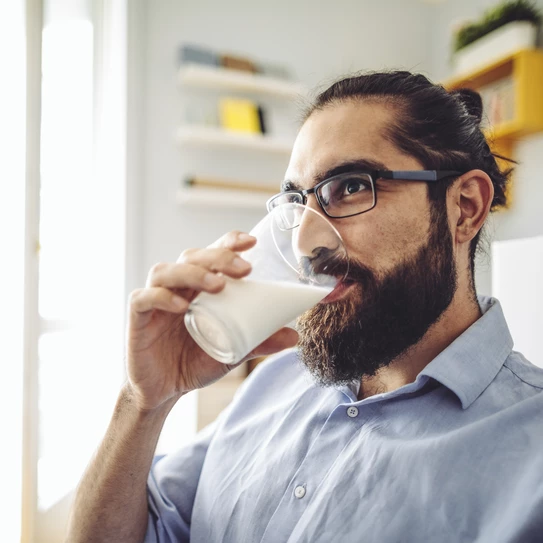 Bärtiger Mann mit Brille trinkt ein Glas Milch